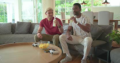 Lemonade arrival starting diverse male pals sipping lemonade grabbing gamepads for gaming on sofa