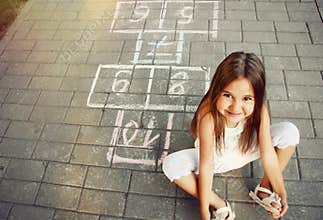 Beautiful cheerful little girl playing hopscotch on playground