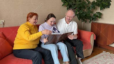 A daughter and her grandparents are sitting on the sofa looking at a family album. orange sofa bright clothes