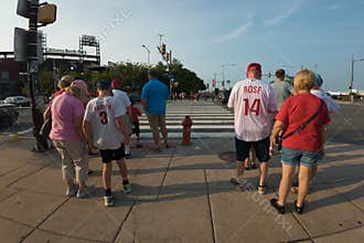 A group of people are standing on a sidewalk, some wearing Philadelphia Phillies jerseys