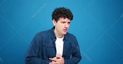 Sad, sick man having stomach pain looking at camera isolated on blue background