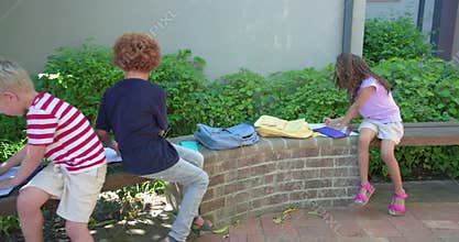 Three school-age children sitting on curved bench sorting papers with purple folder, backpacks