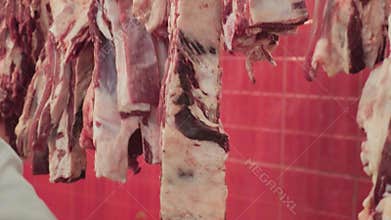 Local butcher stand showing vendor presenting beef cuts to shoppers, with raw steaks, ribs and ham laid out on counter. Scene