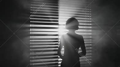 Mysterious Silhouette of a Woman Behind Blinds in a Dark Room with Light Rays