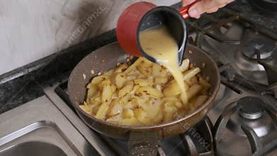 Pouring creamy beaten egg mixture into pan with frying potatoes and onions on gas stove during potato omelet preparation