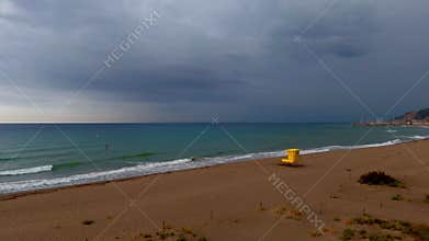 Erial view of yellow lifeguard tower on empty beach as dark storm clouds form over the ocean horizon