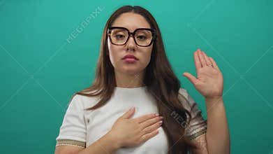 Young woman wearing glasses places hand on chest and raises hand in studio with a serious expression; pledge faith commitment