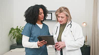 Diverse Female Doctors Discussing Patient Information on a Tablet During a Medical Consultation