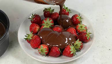 Delicious strawberries being drizzled with rich melted chocolate on a white plate dessert treat