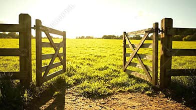 Opening Wooden Gate Leading to Sunlit Meadow with Green Grass in Countryside Scenery at Golden Hour with Clear Sky for Outdoor