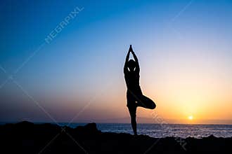 Woman doing yoga tree sunset silhouette