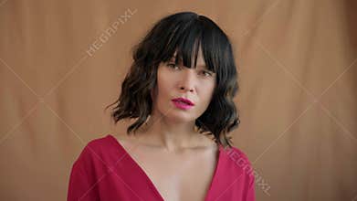 Beautiful fashionable brunette woman with trendy bob haircut, wavy dark hair with bangs, bright make-up, arrogant look and red
