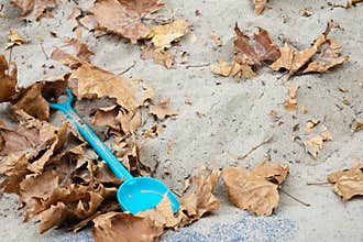 Blue shovel in sandbox with autumn leaves