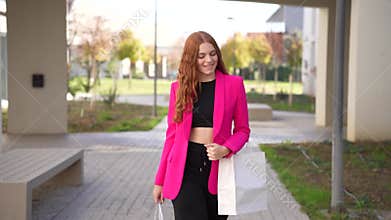 A stylish woman walks gracefully in an urban park, wearing a chic pink blazer and black pants