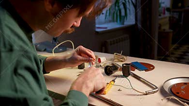 Handyman working at home workshop, using screwdriver and pliers to repair old light bulb socket in vintage lamp.