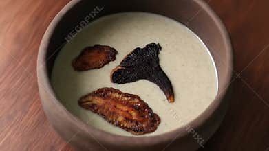 Close-up of a creamy mushroom soup in a rustic wooden bowl, garnished with crisp mushrooms