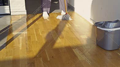 Person Mopping a Shiny Wooden Floor in a Sunlit Kitchen, Performing a Household Cleaning Chore