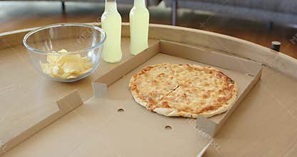 At start camera is moving closer over round wooden table, showing cheese pizza, chips, lemonade