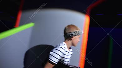 A happy teenage boy with a laser pistol is having fun in a dark laser tag arena.