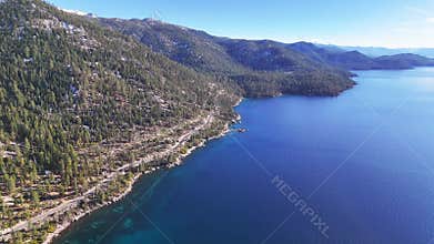 Aerial view of Lake Tahoe coastline at Sand Harbor with winding highway and pine forest under blue sky