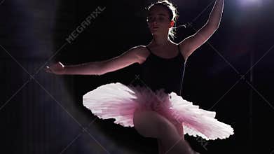 Flexible girl dancing on her pointe ballet shoes in spotlight on black background in studio. Professional young