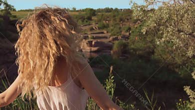 Cheerful and joyful girl with blond curly hair is spinning in place, her curls fall on her face, sincerely smiles and