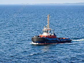 A tugboat navigates on the sea, in the background the coast can be seen