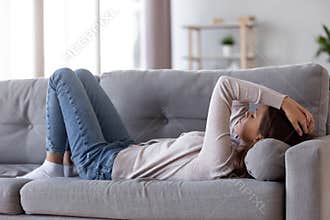 Sad depressed young woman lying on couch feeling headache