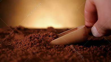 Hand with wooden scoop pushing through cocoa powder
