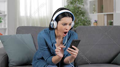 Surprised woman listening to music from cell phone