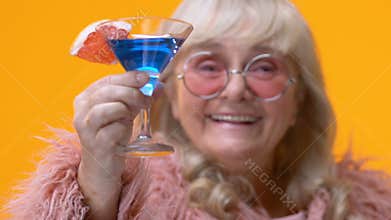 Chic aged lady showing blue cocktail glass in hand, stylish grandmother relax