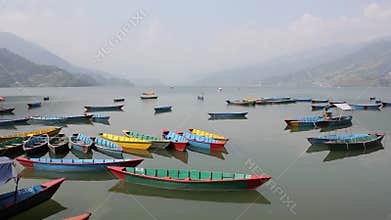 Many empty wooden colored boats on a smooth lake during the day against the backdrop of a mountain valley