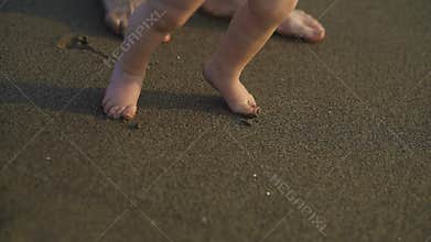 A little baby walking barefoot on the sand. Mother teaches the child to walk.