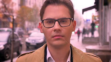 Closeup of adult caucasian man faced to camera looking forward in glasses standing on the street by the road and passing