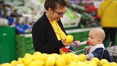 Young mother with baby shopping in supermarket. The child looks at lemon with delight, the development of kids
