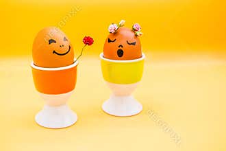 Happy easter eggs with painted drawn cartoon faces on light yellow background. Boy gives girl rose flower. Simplicity concept