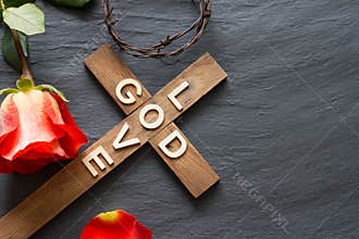 Easter christian wooden cross with an inscription god is love and red rose abstract religion background