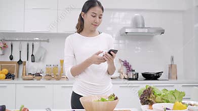 Young Asian blogger woman using smartphone photo post in social media in the kitchen, female making salad at home.