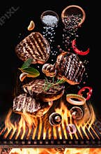 Cooked beef steaks with vegetables and spices fly over the blazing grill barbecue fire