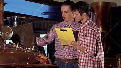 Male brewer and his co-worker examining brewing machine at beer production