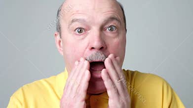 Shocked senior man in yellow shirt is suroprised with news