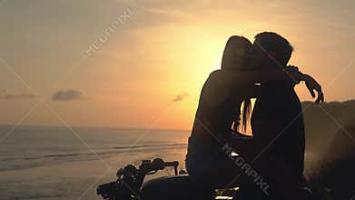Happy lovers on a motorcycle are looking at the bright sunset