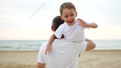 A man carries on his shoulder a happy laughing boy who waves his hands. The concept of family and outdoor recreation