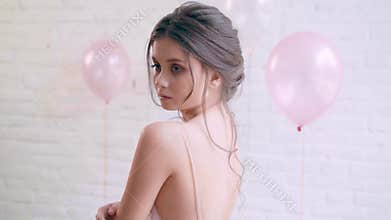 Cute charming girl with a childish face is posing, a model with an ideal tender skin is standing in a free light dress