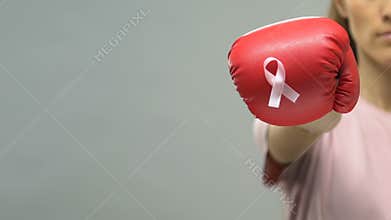 Pink ribbon pinned on boxing glove, concept of woman fighting breast cancer