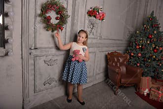 Girl blonde child with a pink teddy bear in hand with a Christmas wreath