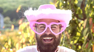 Emotion man with funny hipster pink sunglasses and comic pink hat. Bearded crazy man looking at the camera. Make funny