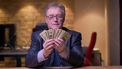 Portrait of senior businessman in formal costume counting money being glad in office.