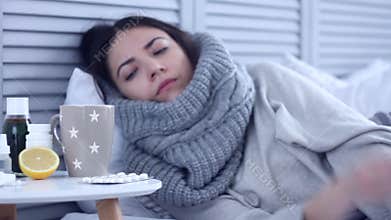 Ill woman lying on bed with flu at grey bedroom