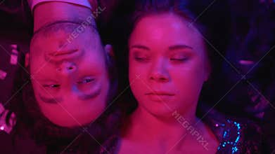 Carefree couple relaxing at rave party lying on floor top view, lights flashing